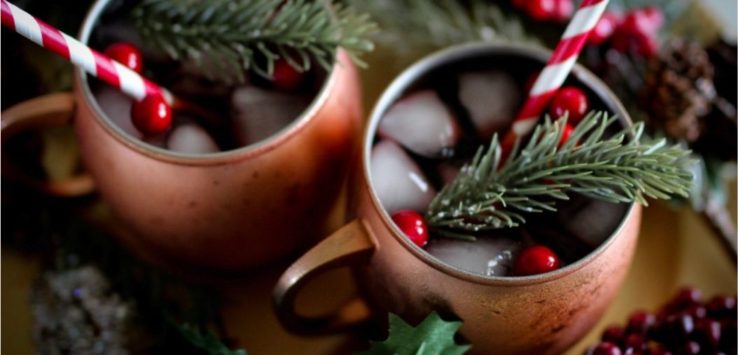Two copper cups of cranberries sangria with a straw and rosemary in each cup.