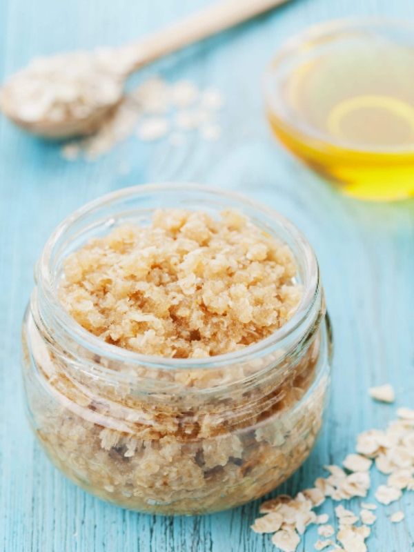 A jar on a blue table filled with oatmeal and sugar and there is a spoon of oatmeal and a bowl of oil behind the jar