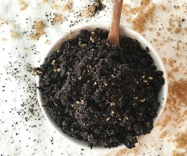 A white bowl with coffee and sugar scrub in it and a wood spoon inside the bowl