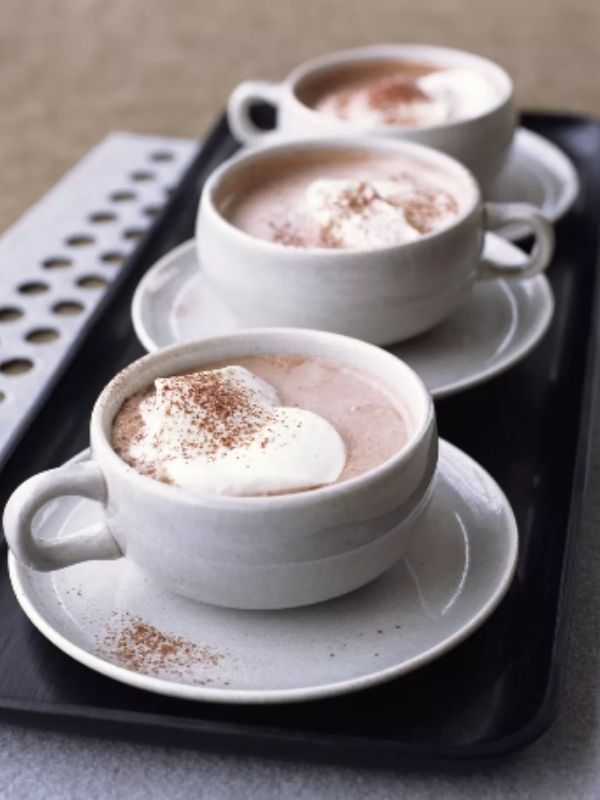 3 row of white mugs filled with hot chocolate and whipped cream